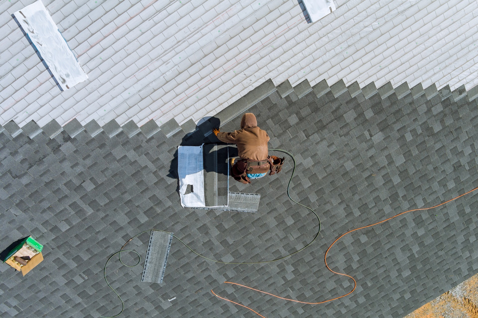 A worker uses an air hammer to nail new roof shingles to bitumen using a top view from above